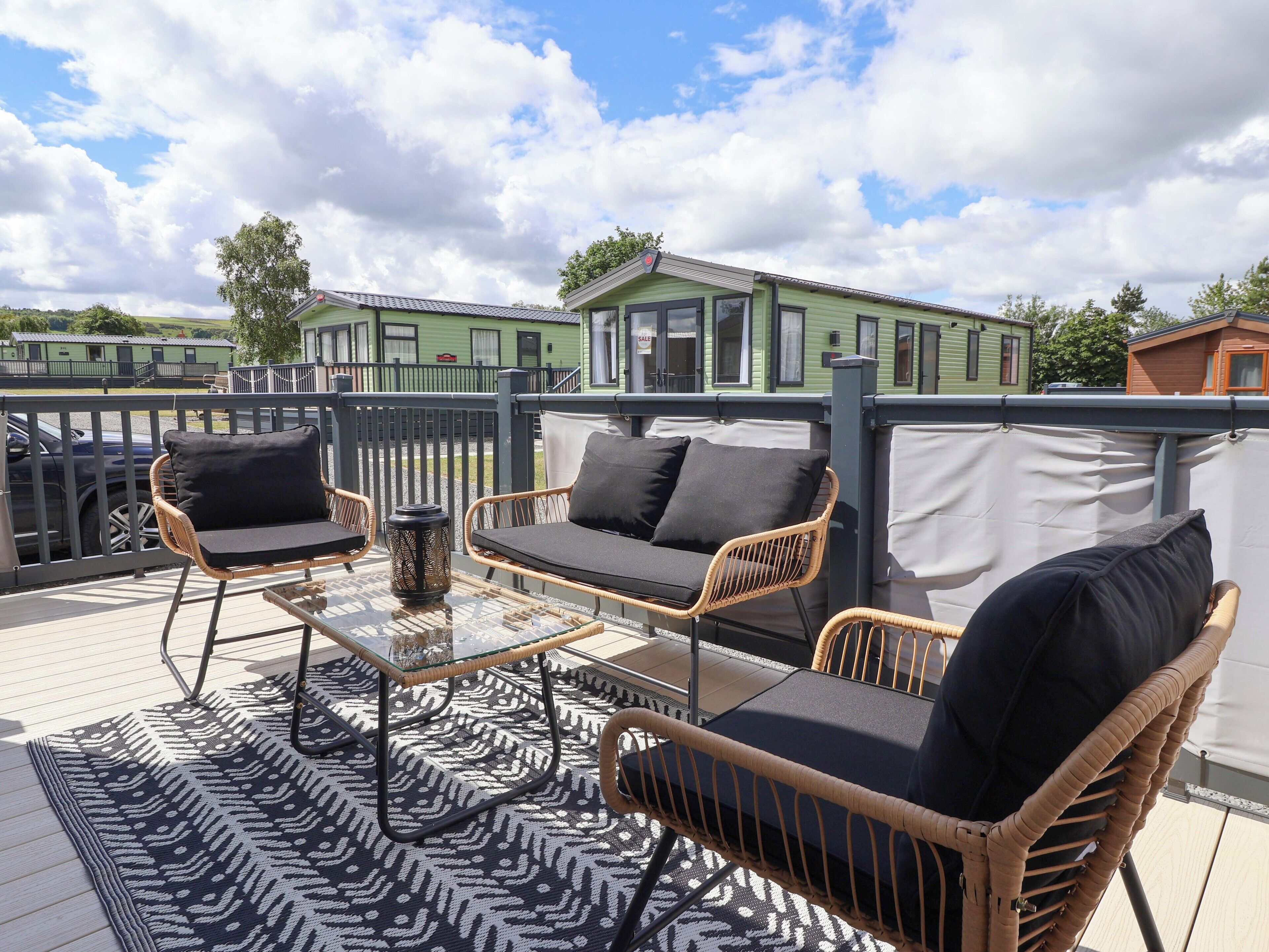 A rooftop patio with wicker furniture, a glass table, and a patterned rug.