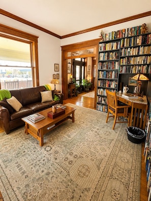 Una sala de estar acogedora con un sofá de cuero marrón, una mesa de centro de madera, una estantería llena de libros y un comedor con una mesa y una silla de madera.