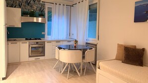 A compact kitchen with a dining table, a built-in oven, and a view of the sea through a window.