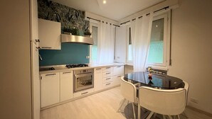 A modern kitchen with white cabinets, a gas stove, an oven, and a dining table with chairs.