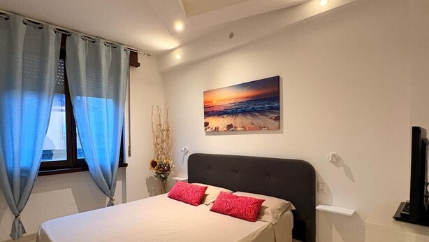 A modern bedroom with a large bed, a painting of a sunset, and a TV on the wall.