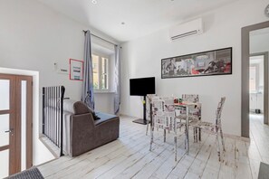En moderne stue med en grå sofa, et spisebord med stole med et avismønster, et fladskærms-tv og et indrammet billede på væggen.