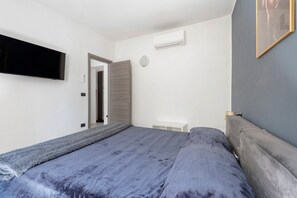 Un dormitorio con cama, televisor de pantalla plana, aire acondicionado y una puerta que da a otra habitación.