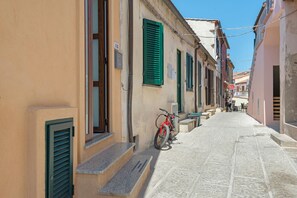 Une rue étroite bordée d’immeubles, un vélo rouge et une personne qui marche.