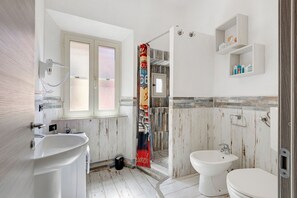 Et badeværelse med bruser, to håndvaske, toilet og et vindue.