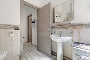Un baño moderno con un lavamanos blanco, un espejo y una puerta de madera.