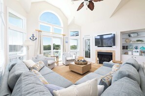 A spacious living room with a large sofa, a coffee table, and a television. There is a fireplace and a bookshelf with decorative items. - Newly Renovated: Pool/Spa, GameRm, Community Perks (Corolla)