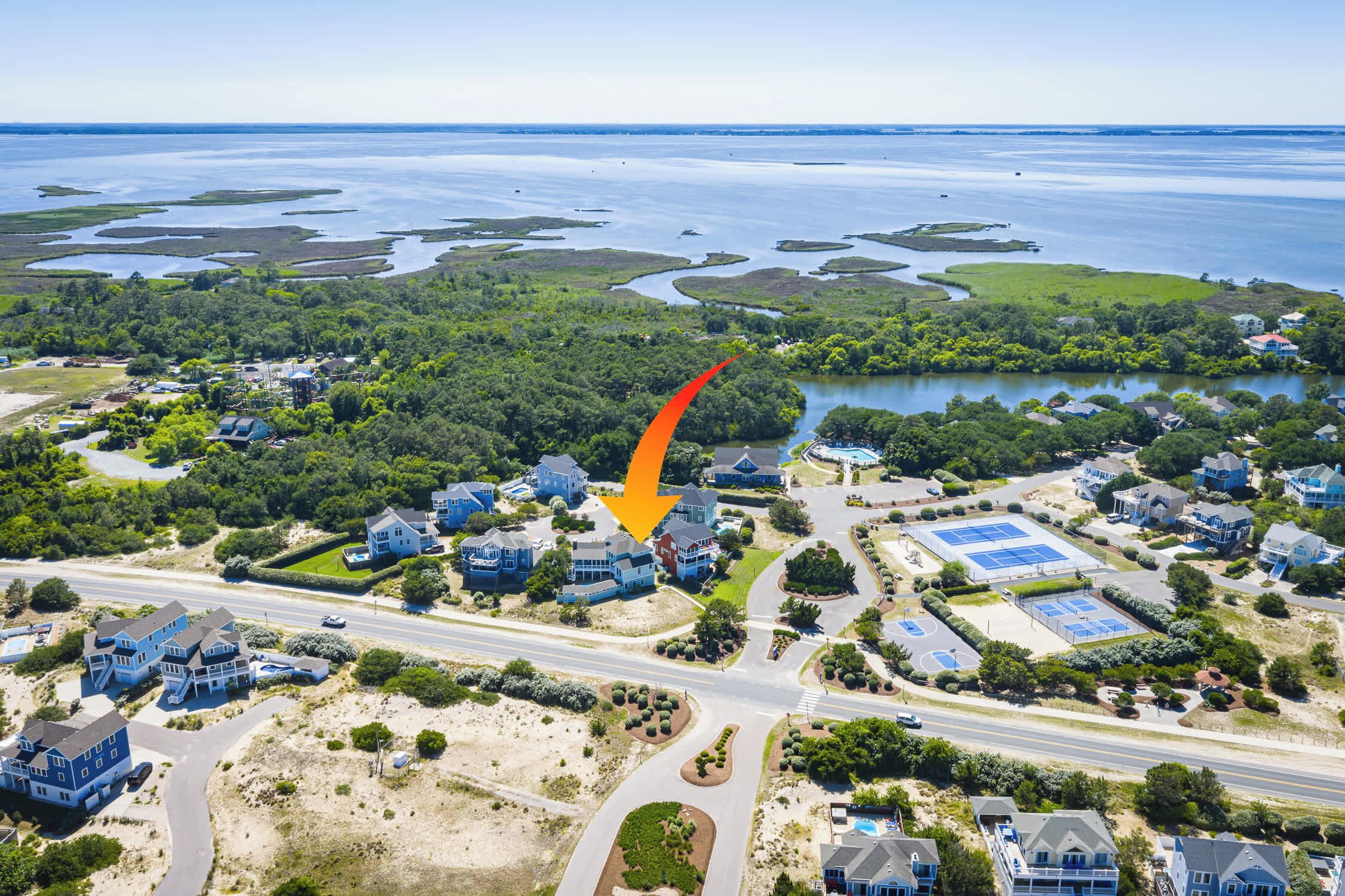 An aerial view of a coastal residential area with houses, roads, and a large body of water.