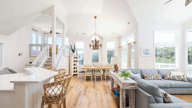 Un'ampia zona giorno con tavolo da pranzo, divano e angolo cottura con piano di lavoro bianco e sedie in vimini.