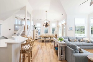 A spacious living area with a dining table, a sofa, and a kitchen area with a white countertop and wicker chairs. - Newly Renovated home with Pool, GameRm, Community Perks (Corolla)