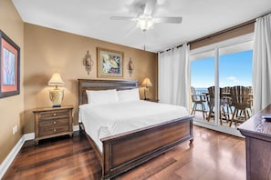 Ein Schlafzimmer mit einem großen Bett, zwei Nachttischlampen, einem Deckenventilator und Meerblick durch eine Schiebetür.
