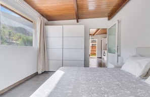 A bedroom with a bed, a window with curtains, a wooden ceiling, and a view of greenery outside. - Country House Near Fataga & Maspalomas (San Bartolomé de Tirajana)