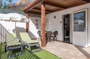 A patio with two lounge chairs, a table, and a covered area with an umbrella.