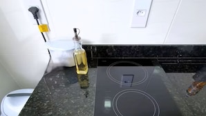 Een keuken met een zwarte inductiekookplaat, een fles olie en een wit apparaat op het aanrecht.