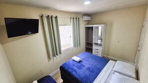 Ein Hotelzimmer mit Bett, Fernseher, Schrank und einem Fenster mit Vorhängen.