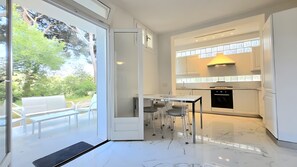 A modern kitchen with white cabinetry, a built-in oven, and a dining area with a glass table and chairs. - Loft 'Oltremare' Apartment with Private Terrace, Wi-Fi & Air Conditioning (Capoliveri)