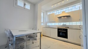 A modern kitchen with white cabinets, a black oven, and a dining area with a table and chairs. - Loft 'Oltremare' Apartment with Private Terrace, Wi-Fi & Air Conditioning (Capoliveri)