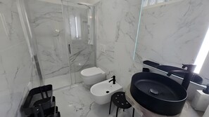 Et moderne badeværelse med en glasbrusekabine, et hvidt toilet, en sort vask og et stort spejl.