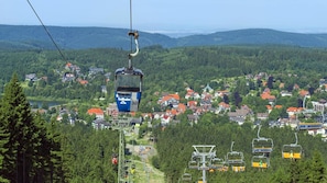 Eine Seilbahnanlage mit Gondeln mit den Nummern 30 und 67, eine Stadt mit roten Dächern und ein bewaldeter Hintergrund.