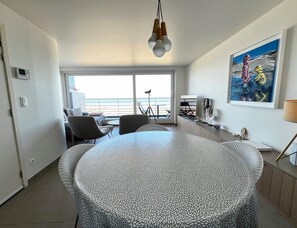 Ein modernes Wohnzimmer mit rundem Tisch, einem Balkon mit Blick und einem Bild an der Wand.