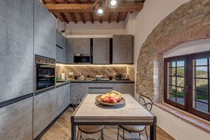 Una cocina moderna con pared de piedra, techo de madera y una mesa de comedor con fruteros.