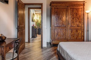 Una habitación con un armario de madera, una cama con colcha, una mesa de comedor con sillas y un pasillo que conduce a otra habitación.