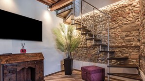 A modern interior with a wooden cabinet, a large potted plant, a purple ottoman, a staircase against a stone wall, and a flat-screen TV mounted on the wall. - Elegant Tuscan Home in Chianti Near Florence (Sant'Andrea in Percussina)