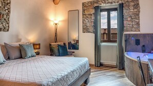 A bedroom with a large bed, a bedside table, a mirror, a stone wall, a window, and a bathroom with a bathtub. - Elegant Tuscan Home in Chianti Near Florence (Sant'Andrea in Percussina)
