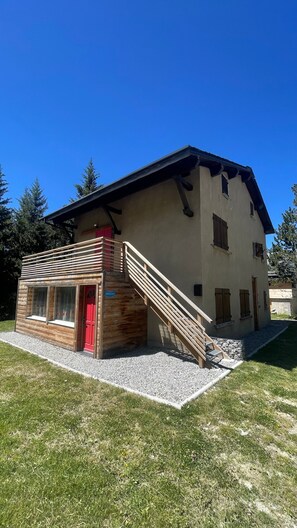 Ein zweistöckiges Gebäude mit einer Holztreppe, die zu einer roten Tür, einem Balkon und einer Schotterauffahrt führt.