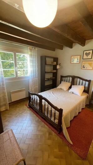 Ein Schlafzimmer mit einem hölzernen Bett, einem Heizkörper, einem Fenster mit Vorhängen, einem Bücherregal und gerahmten Bildern an der Wand.