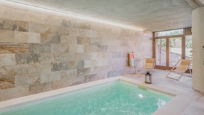 A swimming pool with stone walls, a tiled floor, and two lounge chairs.
