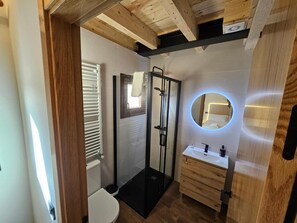 A modern bathroom with a glass shower enclosure, a round mirror with underglow lighting, and wooden cabinetry.