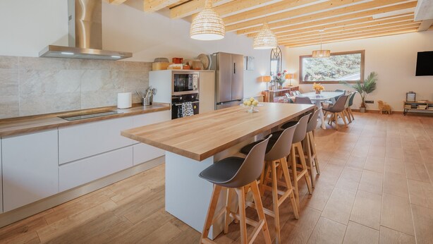 A modern kitchen with wooden beams, a central island with bar stools, stainless appliances, and a large window.