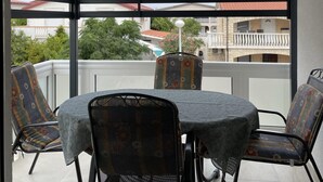 Ein überdachter Außenbereich mit Tisch und Stühlen, Blick auf Wohnhäuser und einem Balkongeländer.