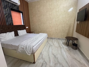 Habitación de hotel con cama, una mesita, televisor montado en la pared y ventana con cortinas.
