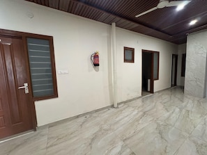 A corridor with marble flooring, wooden doors, and a fire extinguisher mounted on the wall. - Deluxe Hotel Prince (Mohali)