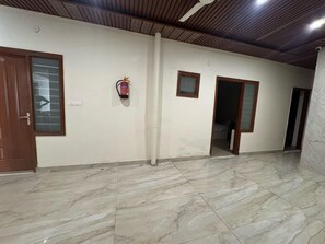 A hallway with marble flooring, wooden doors, a ceiling fan, and a fire extinguisher. - Deluxe Hotel Prince (Mohali)