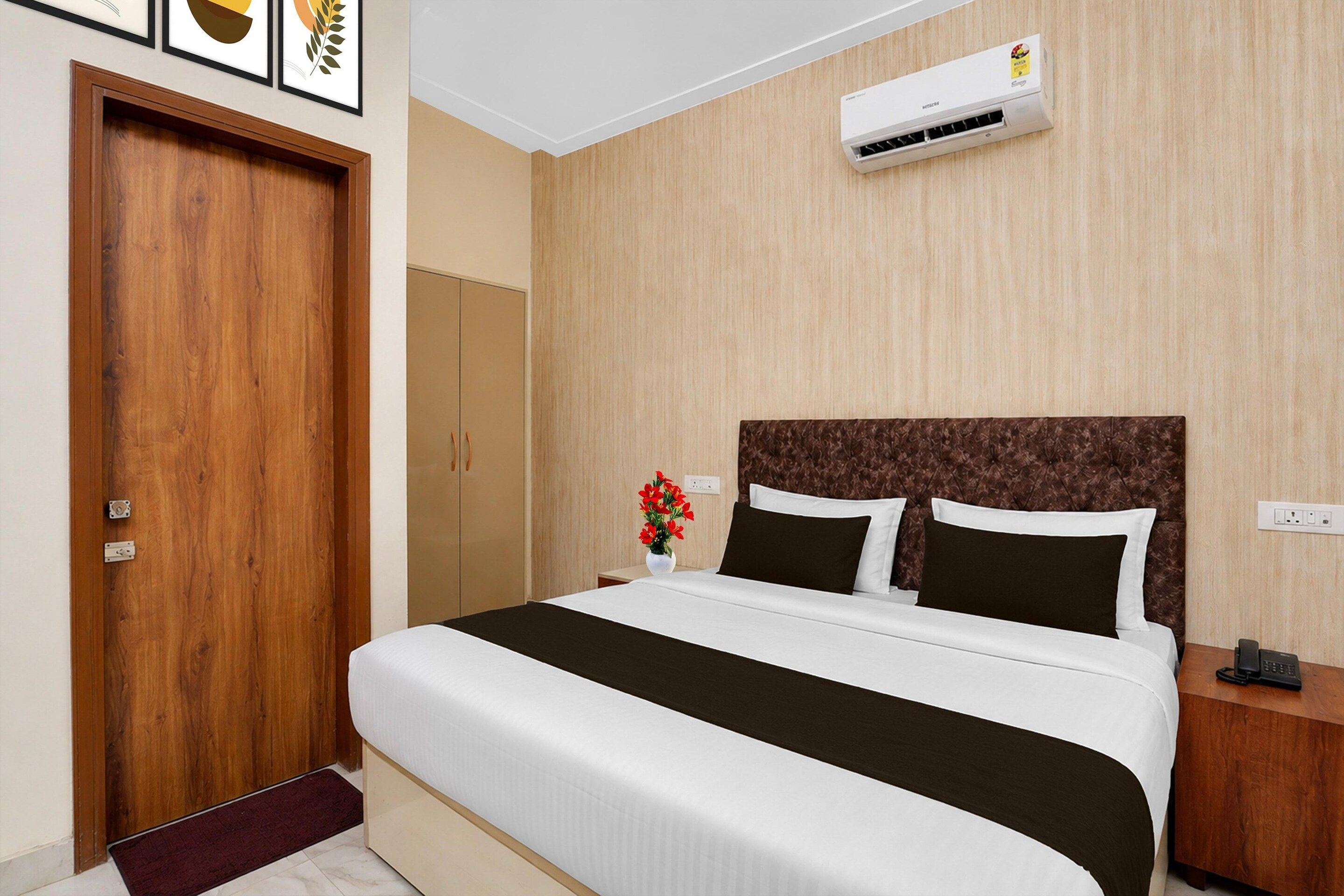 A hotel room with a bed, bedside table, nightstand, and an air conditioning unit.