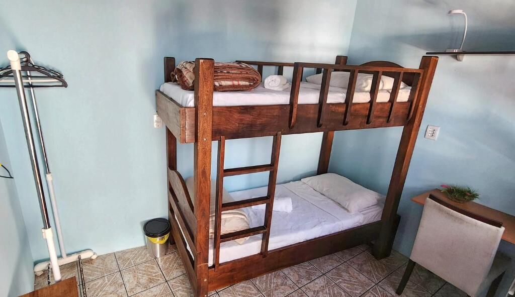 Een stapelbed met een ladder, een tafeltje en een prullenbak in een kamer met lichtblauwe muren.
