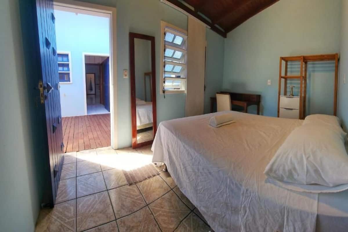 A bedroom with a bed, a desk, and a chair. There is a door leading to another room.
