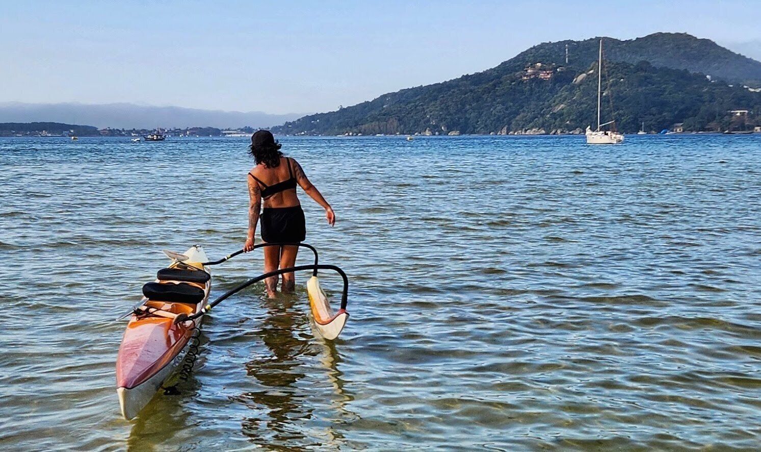 A person in a kayak on a body of water with a mountainous landscape in the background.
