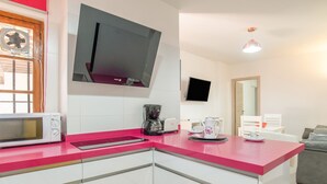 Una cocina moderna con encimera rosa, armarios blancos, microondas, cafetera y televisor de pantalla plana montado sobre la encimera.
