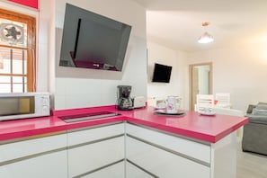 Eine moderne Küche mit rosa Arbeitsplatte, weißen Schränken, einer Mikrowelle, einer Kaffeemaschine und einem flachbildfernseher, der über der Arbeitsfläche angebracht ist.