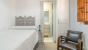 Un dormitorio con cama, una silla, un armario y una puerta que da a un baño.