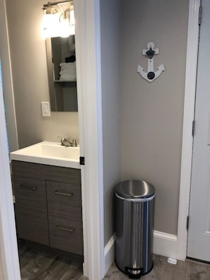 Une salle de bain avec un lavabo, un miroir et une poubelle.
