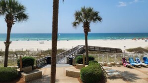 A beach view with palm trees, a wooden deck, and beach chairs. - Pelican Pointe - Beautiful Beach Front Condo! 2nd Floor, 3 Bedroom (Orange Beach)