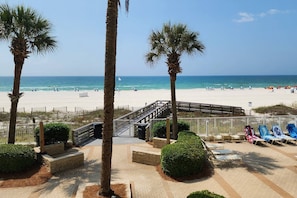 Blick auf einen Strand mit Palmen, einer Holzterrasse und Liegestühlen.