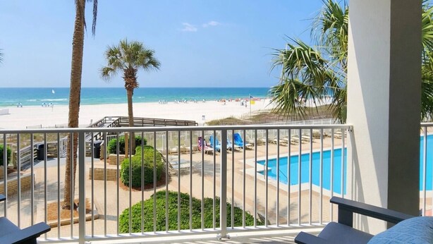 A balcony with a view of a beach, a pool, and palm trees. - Pelican Pointe - Beautiful Beach Front Condo! 2nd Floor, 3 Bedroom (Orange Beach)