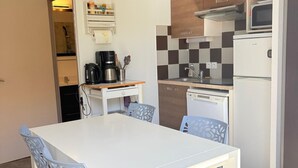 Ett kompakt kök med ett vitt bord, blå stolar, en kaffemaskin och en mikrovågsugn.