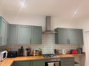 A kitchen with teal cabinets, a gas stove, a microwave, and various kitchen utensils. - Boho Retro 4-bedroom house in charming Headingley for your Leeds stay (Leeds)